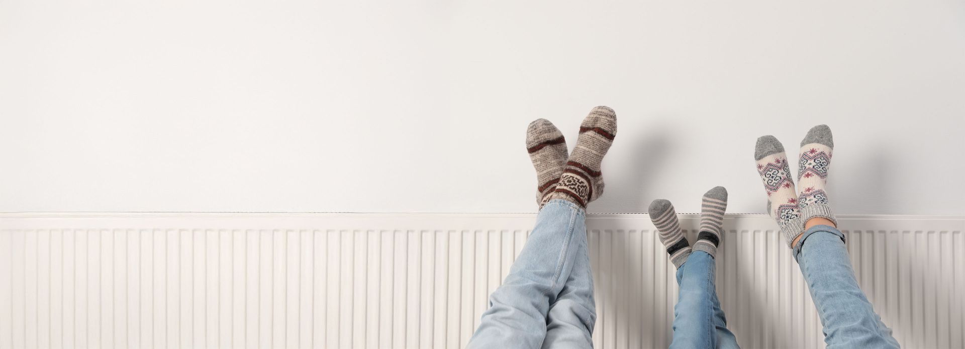 3 Menschen lehnen ihre Füße an eine Heizung. Sie haben Stricksocken an.