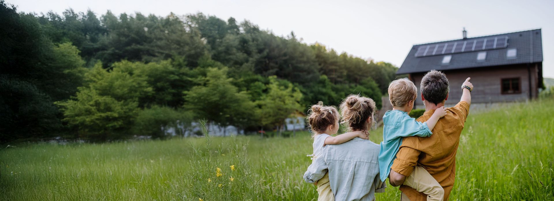 Junge Familie steht vor ihrem neuen Zuhause mit einer modernen PV-Anlage auf dem Dach