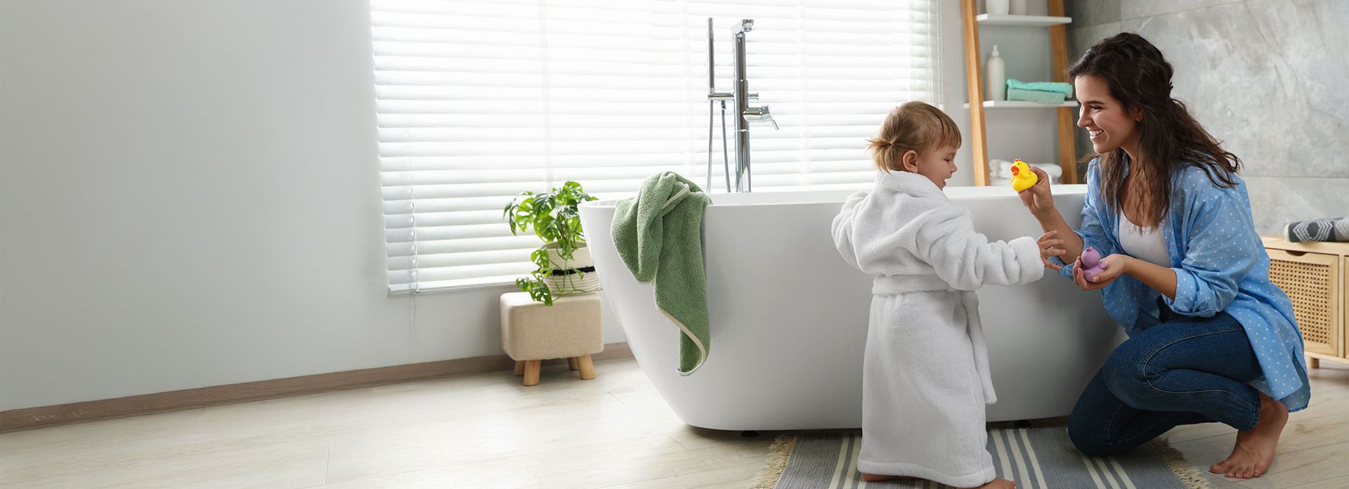 Junge Mutter mit ihrer Tochter stehen im modernen Badezimmer und machen sich bereit für ein Bad in der Badewanne